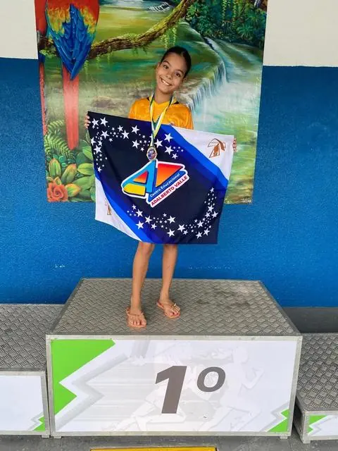 Lelê no primeiro lugar do pódio segurando a bandeira da equipe